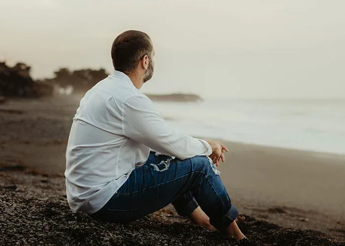 Man sitting alone on beach contemplating past decisions