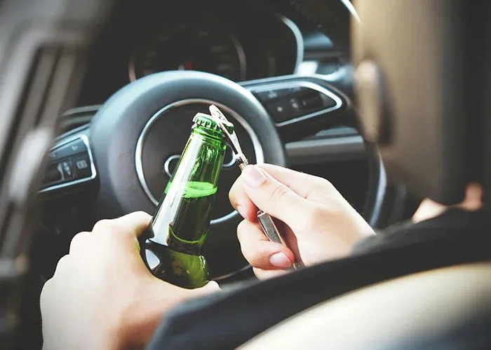 Person opening beer bottle in car showing risky behavior