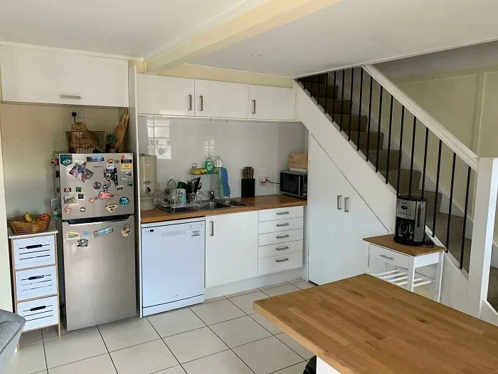 Small kitchen under stairs with white cabinets and wooden countertops