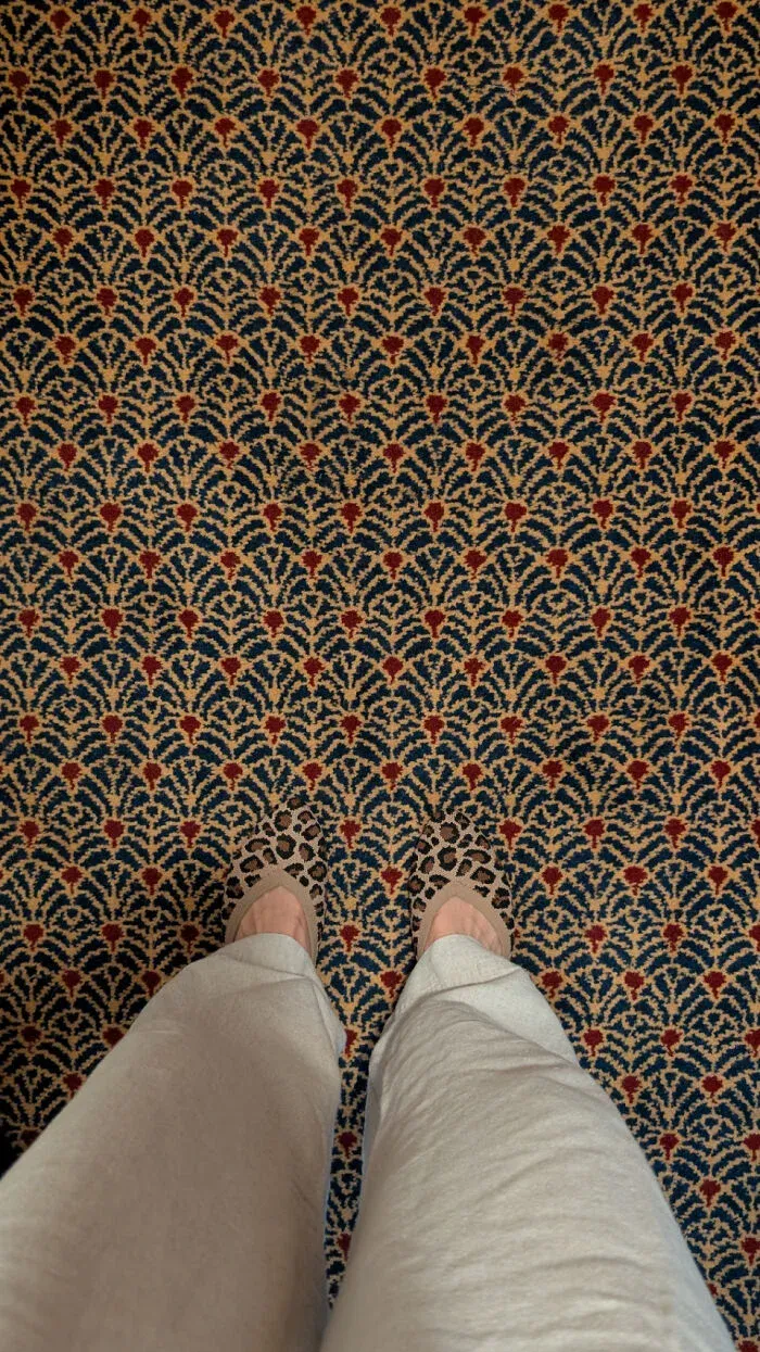 Person standing on patterned carpet blending with pants and shoes detail