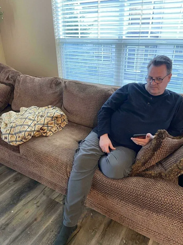 Man sitting on a couch with a hidden cat camouflaged in the cushion