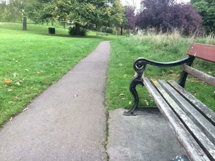 Park bench with armrest blending into the nearby path and grass detail