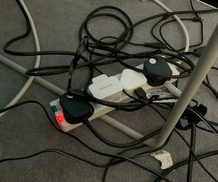 Tangled black charging cables plugged into power strip on carpet