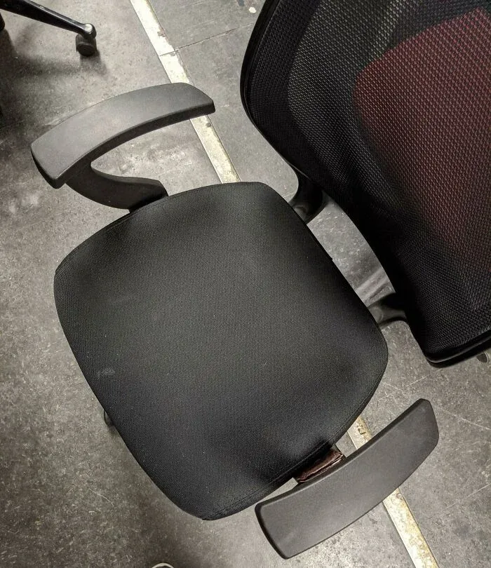 Black office chair with worn fabric and armrests on concrete floor